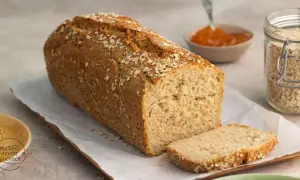 Frisch gebackenes Haferbrot, bestreut mit Haferflocken. Ein Glas Haferflocken und Marmelade daneben deuten auf ein leckeres Haferbrot Rezept hin.