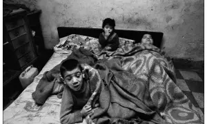 Bambini in un letto, un piccolo è seduto con le dita in bocca, un altro è sdraiato. Un'immagine toccante, una delle **Letizia Battaglia foto famose**.