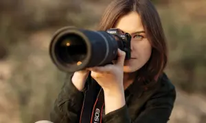 Kobieta z aparatem Canon EOS R7 w rękach, gotowa do uchwycenia idealnego ujęcia. Jej skupienie zdradza pasję do fotografii mody.