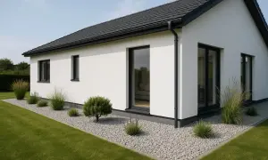 Nowoczesny biały dom z czarnym dachem i oknami. Wokół domu zadbany ogród z trawami ozdobnymi i kamieniami, tworzący najtańszą opaskę wokół domu.