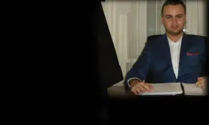 Mężczyzna w garniturze siedzi przy biurku z dokumentami.