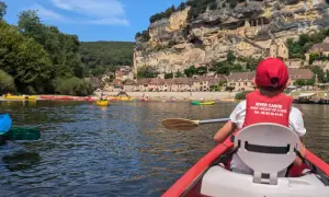 Enfant en canoë rouge, gilet de sauvetage "River Canoe", pour une visite insolite autour de Sarlat, avec des falaises et des maisons troglodytes en arrière-plan.
