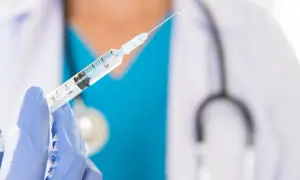 Lekarz w niebieskiej rękawiczce trzyma strzykawkę z kroplą szczepionki. Dostępne są szczepienia na Sri Lance.