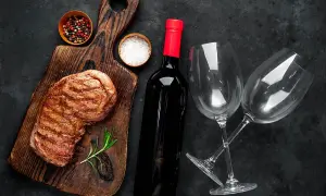 Grillowany stek, butelka wina z regionu Puglia, dwa kieliszki, sól i pieprz na drewnianej desce.