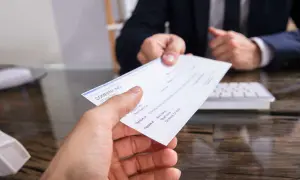 Mancata riscossione di assegno bancario dopo rogito notarile. Mano che porge un assegno, con un uomo in giacca e cravatta sullo sfondo.