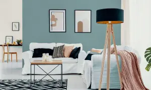 Nowoczesny salon z białymi sofami, stolikiem kawowym i lampą na drewnianym statywie. Ściana w odcieniu **kolor lazurowy** tworzy spokojną atmosferę.