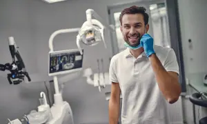Uśmiechnięty dentysta w gabinecie, gotowy do pracy. Zastanawiasz się, ile trwa plombowanie zęba? To zależy od przypadku, ale zazwyczaj krótko!
