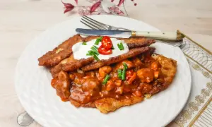 Pyszny placek po węgiersku z gulaszem, śmietaną i papryczką chili na białym talerzu.