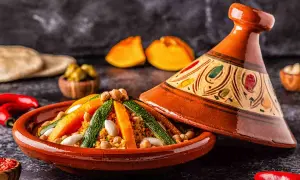 Un saporito cous cous tajine con verdure colorate e ceci, servito in un tradizionale piatto di terracotta decorato.