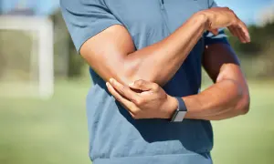 Mężczyzna trzyma się za bolący łokieć, nosząc zegarek sportowy.