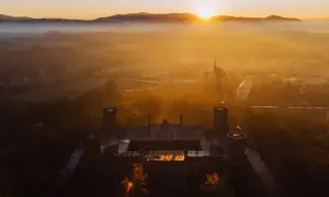 Zamek otoczony mgłą, skąpany w ciepłych promieniach **golden hour**. Słońce wschodzi nad wzgórzami, malując niebo na złoto.