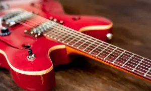 Czerwona gitara elektryczna na drewnianym tle. Idealna do nauki gry na gitarze elektrycznej.
