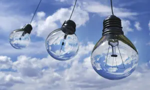 Trzy żarówki wiszące na tle błękitnego nieba z chmurami. W ich wnętrzu odbija się niebo, symbolizując moc bierną, co to jest – potencjał do działania.