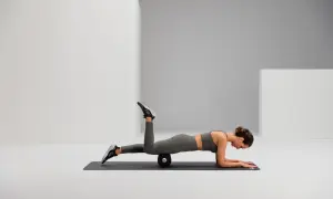 Frau auf einer Matte mit Foam Roller unter dem Oberschenkel, um Hohlkreuz wegtrainieren.
