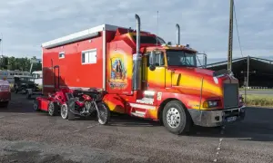 Un poid lourd américain rouge et jaune, customisé avec une peinture de femme amérindienne, est garé à côté d'une moto rouge.