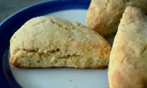 Tre gyllene scones, bakade med bakpulver, ligger på en tallrik med blå kant.