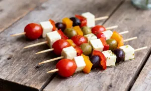 Des brochettes apéro colorées avec des tomates cerises, des cubes de fromage, des poivrons et des olives sur une table en bois.