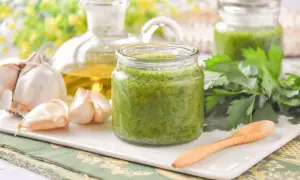 Un frasco de salsa mery verde vibrante, con ajo, aceite de oliva y perejil fresco alrededor.