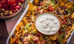 Nachos caseros con queso derretido, carne, frijoles, jalapeños y un tazón de crema agria.