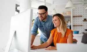 Coppia sorridente davanti al computer, scopre come funziona la banca ore per ottimizzare il lavoro.