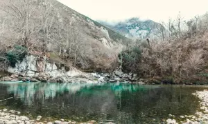 El río turquesa fluye sereno, reflejando árboles desnudos y montañas neblinosas. Un paisaje que evoca la paz de la olla de San Vicente.