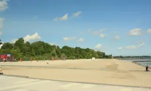 Sonniger **Stralsund Strand** mit Spielplatz, Liegewiese und Blick aufs Wasser. Ein Mann macht ein Foto.