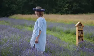 Uśmiechnięta Nico w wianku z lawendy, otoczona fioletowym polem. Obok drewniany domek dla owadów.