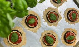 Kleine Aubergine-Pizza-Häppchen mit Tomatensoße, Käse und frischem Basilikum auf einem Backblech.