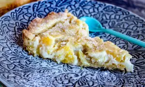 En bit ananaspaj med pudersocker på en mönstrad tallrik. Perfekt för ett ananaspaj recept.
