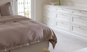 Ett sovrum med en stor säng med brunt sängkläder och en vit garderob i klassisk inredningsstil.