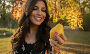 Donna sorridente tiene una pera gialla, uno dei cibi che fanno fare la cacca subito, in un parco autunnale.