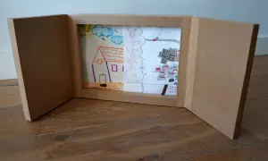 Un kamishibai casero muestra dibujos infantiles: una casa, un paisaje rural y un pueblo con un tren.