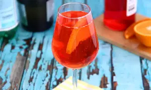 En Aperol Spritz, Italiens nationaldryck, med apelsinskiva i glaset. Bakom syns flaskor och en apelsinhalva.
