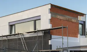 Budowa domu z widoczną warstwą izolacji, która zapewnia **efektywność energetyczną**. Widać cegły, styropian i okna.