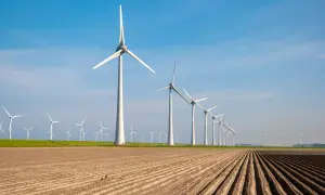 Rząd białych turbin wiatrowych na tle błękitnego nieba, z zaoranym polem w pierwszym planie.