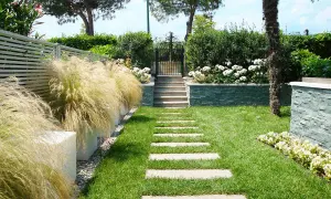 Un bellissimo giardino progetto con un sentiero di lastre di pietra, erba verde, cespugli fioriti e un muretto in pietra.