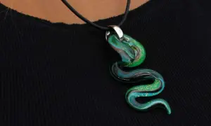 Un serpente sinuoso de **colgante de cristal de Murano** en tonos verdes y azules, con destellos dorados, descansa sobre una tela negra.