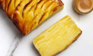 Une tranche de tarte aux pommes, dorée et caramélisée, à côté d'une autre tranche montrant la texture fine des pommes. Un petit pot de caramel est aussi visible.