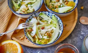 Erfrischender Chicorée-Salat mit Orangenstücken und Nüssen in blauen Schalen, serviert auf einem Holztablett.