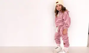 Dziewczynka w różowym welurowym dresie i czapce, białe buty sportowe.