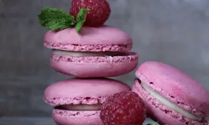 Różowe makaroniki z malinami i miętą ułożone na drewnianym blacie.