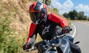 Motocyklista w czerwono-czarnym kasku i kurtce jedzie po krętej drodze.