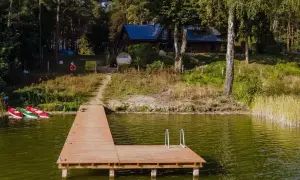Drewniany pomost nad jeziorem w Chojnicach, obok trzy kajaki. W tle dom wśród drzew.