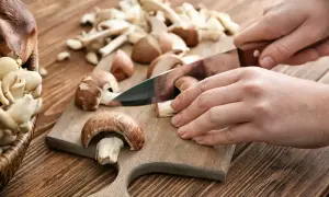Ręce kroją pieczarki na desce. Niskie pieczarki kcal to zdrowa przekąska.