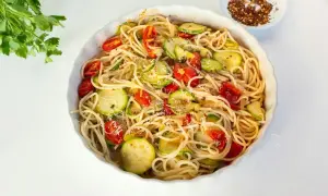 Makaron spaghetti z cukinią i pomidorkami koktajlowymi, posypany parmezanem.