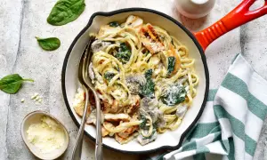 Kremowy makaron z kurczakiem, szpinakiem i grzybami w patelni, posypany parmezanem.