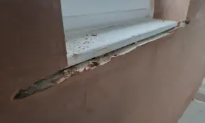 Fensterlaibung verputzen: Rauer Putz umrahmt ein weißes Fensterbrett, das mit kleinen Putzbrocken übersät ist.