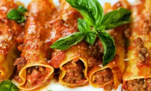Cannelloni di carne ricetta della nonna, ripieni di ragù e conditi con sugo rosso e basilico fresco.