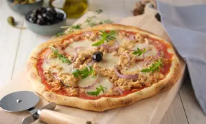 Une délicieuse pizza au thon, garnie de mozzarella fondante, d'oignons rouges et de roquette fraîche, prête à être découpée.