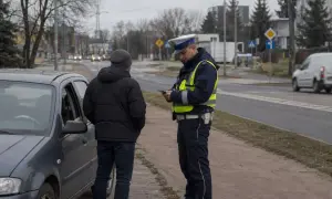 Policjant kontroluje kierowcę stojącego przy samochodzie. Dowiedz się, co grozi za jazdę bez prawa jazdy po jego zatrzymaniu.